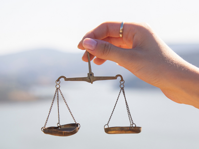 Image of a hand holding a balanced scale with water in the background.