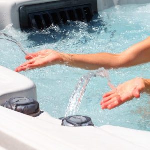 Image of a person's hands reaching out under 2 streams of fountain in a hot tub.