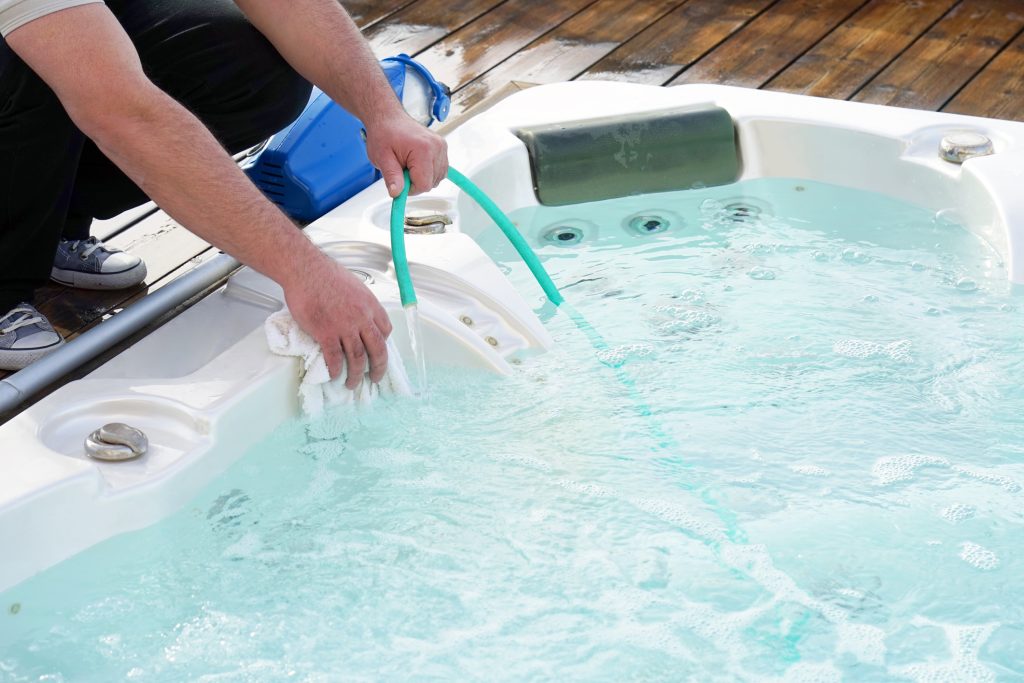 Image of a man bending over a hot tub filling it with hose water.