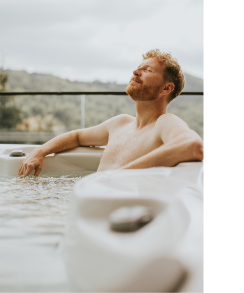 A middle aged man sitting in an outdoor hot tub smiling with his eyes closed.