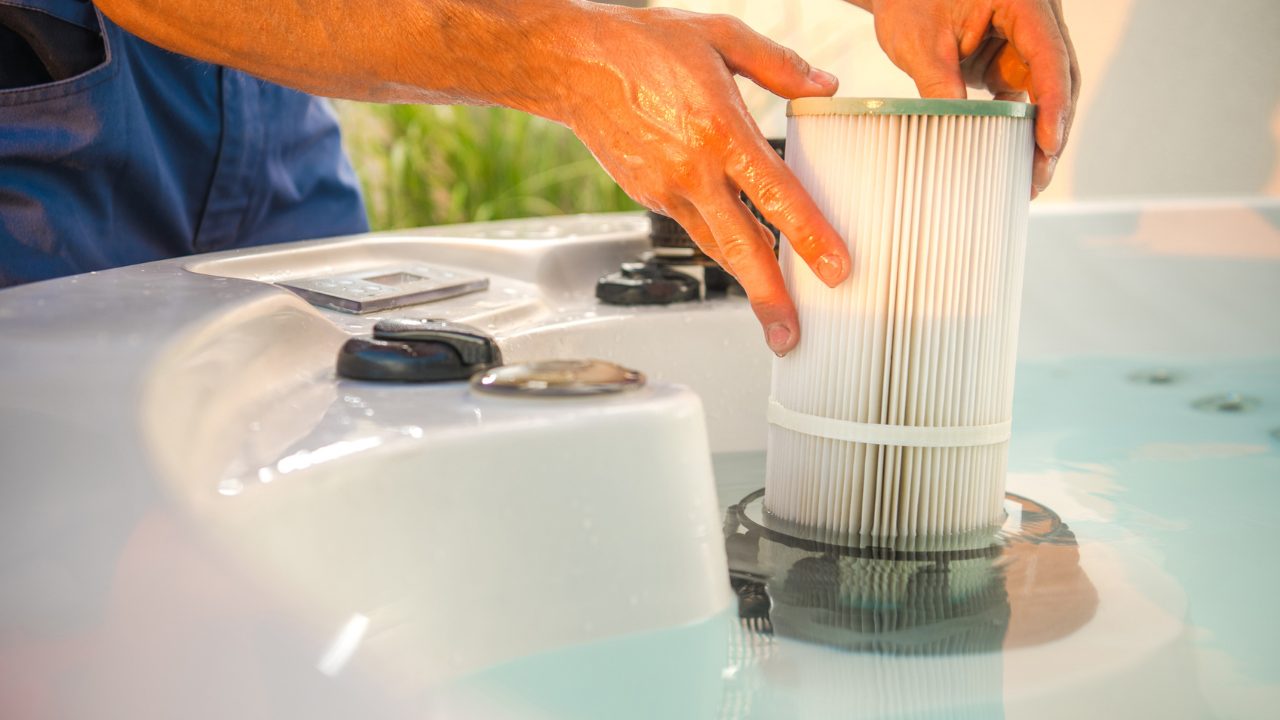 Man's hands pulling a hot tub filter out of its spot in the hot tub.