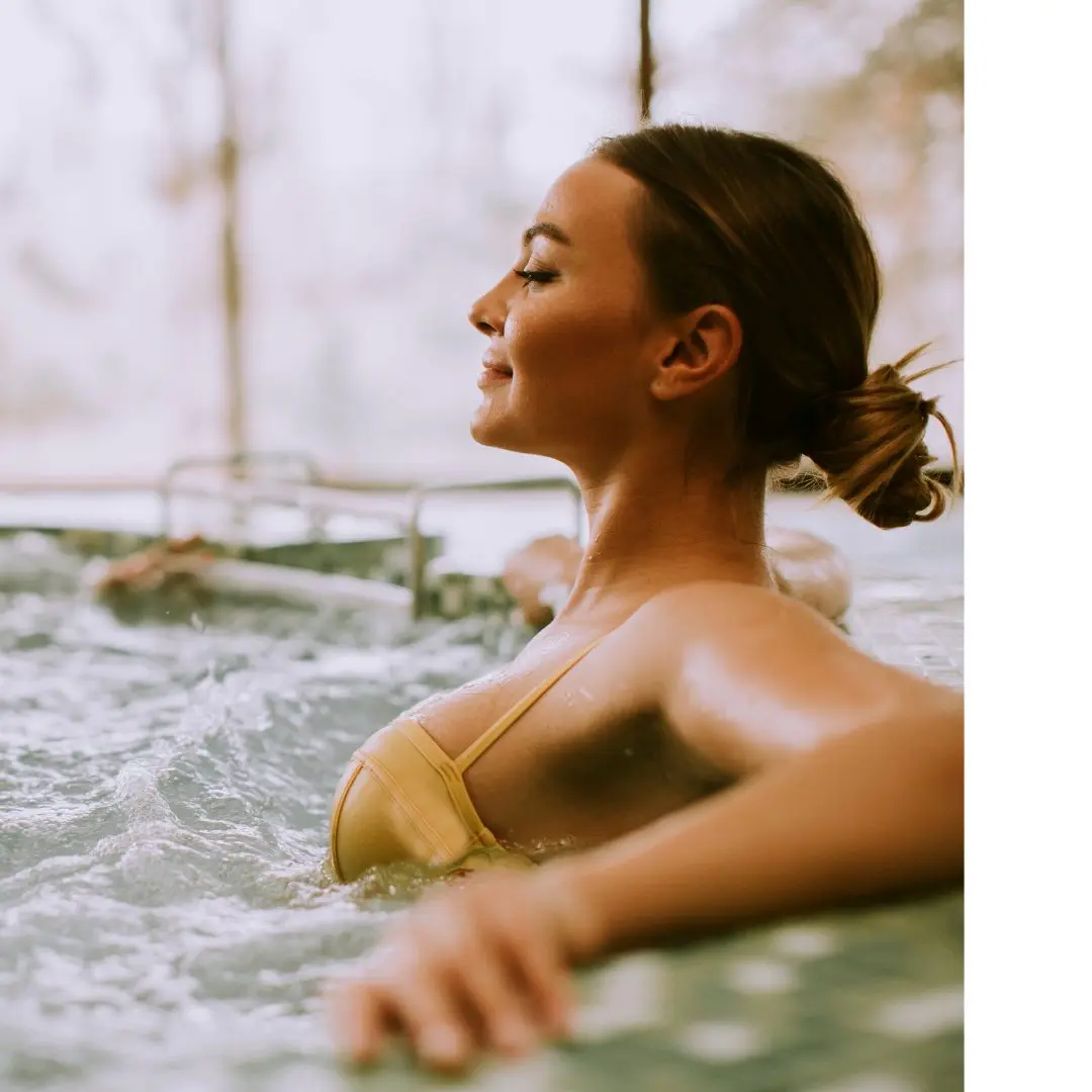 A woman sits in her swim spa with her hair in a bun and her eyes closed.