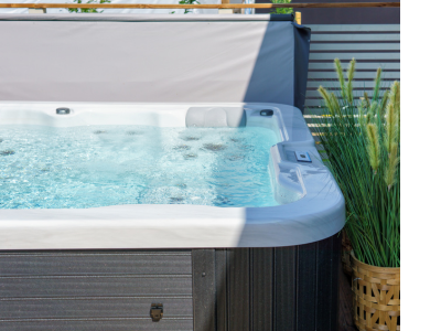 Shot of the side of a hot tub. There is a fence behind it and a plant alongside it.