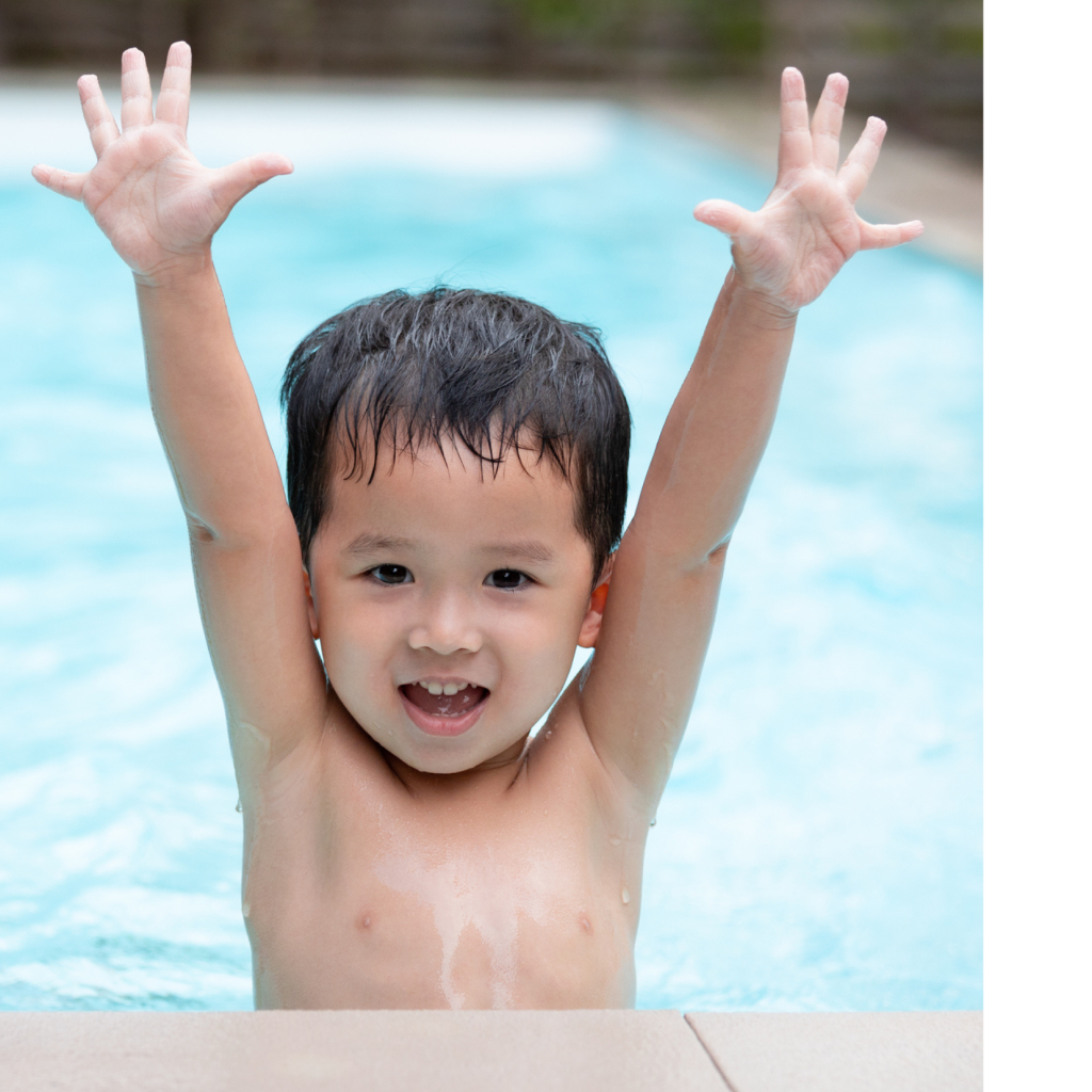 A young boy poses with his arms up in excitement in an outdoor pool