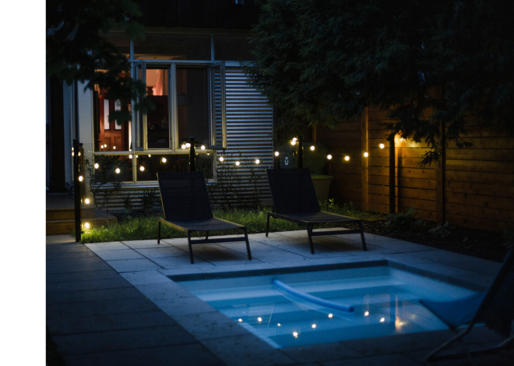 An outdoor pool is lit up with string lights and underwater LEDs