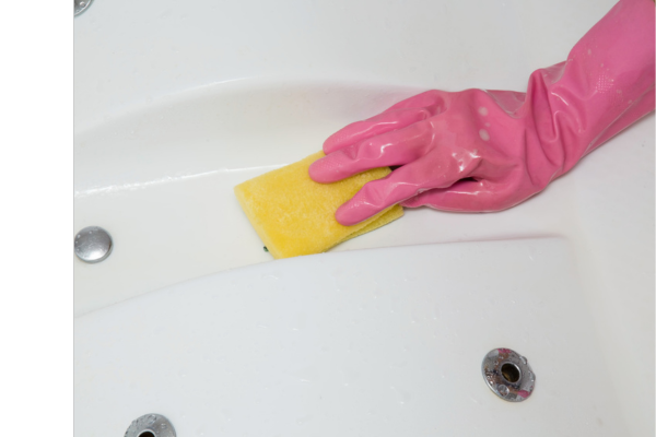 A gloved hand cleans the shell of a swim spa with a yellow sponge