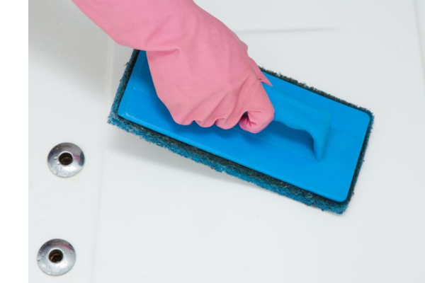 A gloved hand uses a scrubber to clean the shell of a hot tub.