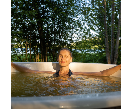 A woman sits in the hot tub with her arms outstretched on the edge of the hot tub.