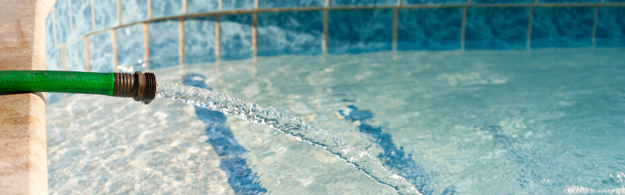 A hose hangs on the side of a pool filling up the pool with water