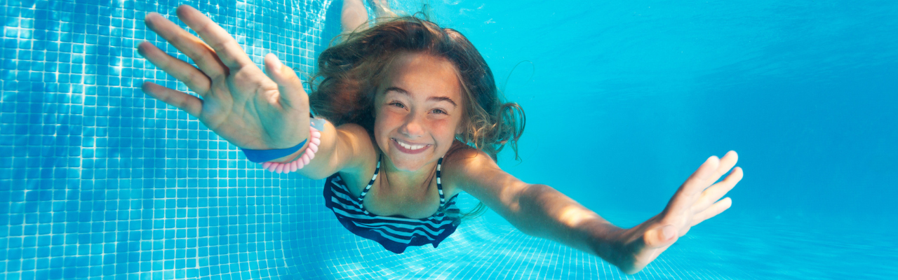 A young girl dives deeper into the pool water. This photo is shot from underwater