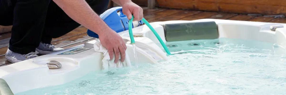 Hot tub being scrubbed with a towel and rinsed with a hose — cleaning before drain and refill or seasonal shutdown.